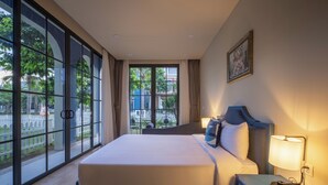 Ein Hotelzimmer mit einem großen Bett, einem Nachttisch mit Lampe und Blick durch große Fenster nach draußen.