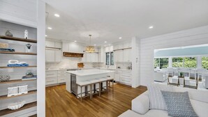 A modern kitchen with white cabinetry, a large island, and wooden flooring. - 7BR Estate · One Block to Ocean · Sleeps 22 (Falmouth)