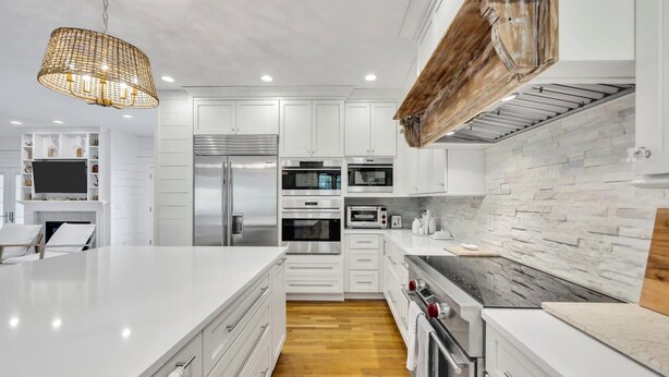 A modern kitchen with white cabinetry, stainless steel appliances, a large island, and a hanging light fixture. - 7BR Estate · One Block to Ocean · Sleeps 22 (Falmouth)