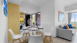 Una sala de estar moderna con un sofá gris, sillas blancas y una mesa de comedor preparada para cuatro comensales.