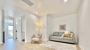 A spacious living room with a light grey sofa, a wooden chair, and a floor lamp. - Kanab Desert Oasis - Pool, Hot Tub + Pickleball (Kanab)