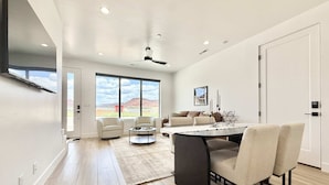 A modern living room with a large window, a dining area with a round table, and a sofa. - Kanab Desert Oasis - Pool, Hot Tub + Pickleball (Kanab)