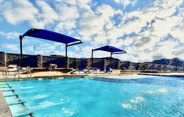 A swimming pool with blue umbrellas, lounge chairs, and a stone wall.