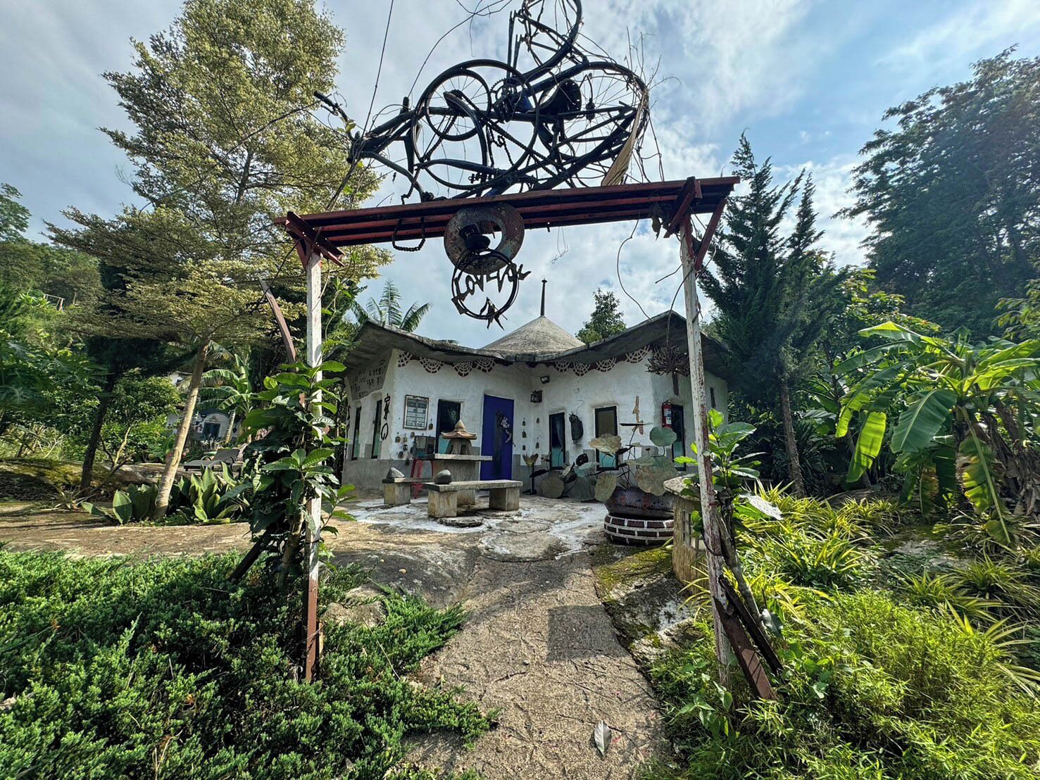 Una casa rústica con techo de paja, rodeada de exuberante vegetación y cielo despejado.