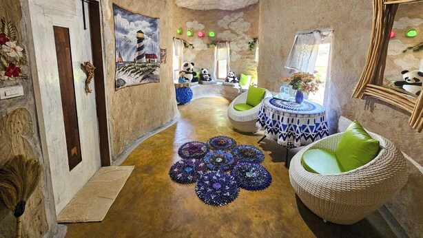 Un interior rústico con pared de piedra, una mesa redonda con mantel estampado, muebles de mimbre y una alfombra decorativa.