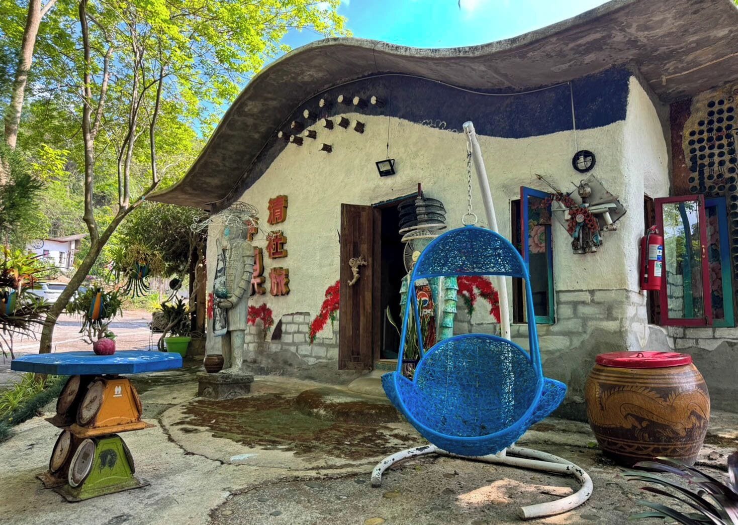Un edificio rústico con techo curvo, una hamaca azul colgante y una gran urna decorativa.
