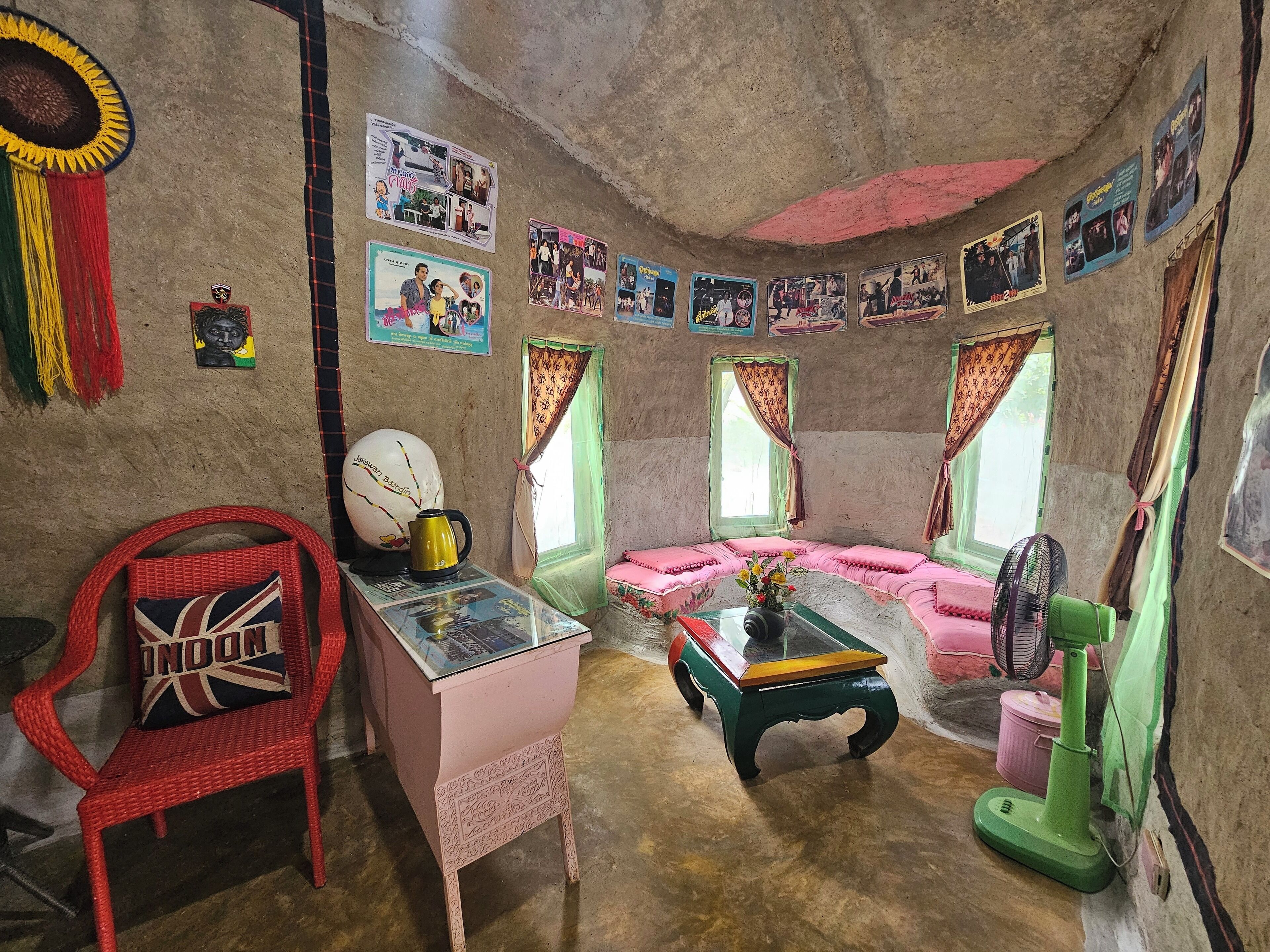 A room with a sofa, a table with a kettle, a chair, and a fan.