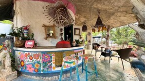 Un rústico espacio de bar con un mural colorido, taburetes de madera y adornos colgantes.
