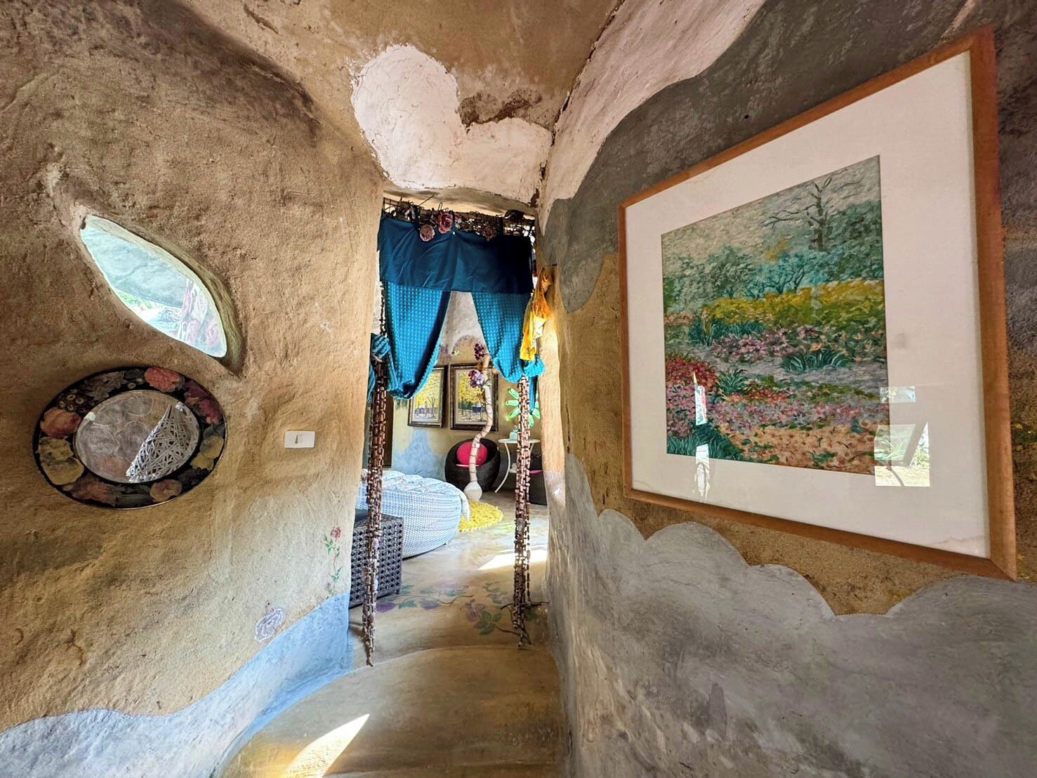 Un interno rustico e stretto, con una scala che conduce a una stanza. Le pareti sono strutturate e irregolari, con un quadro appeso a destra.