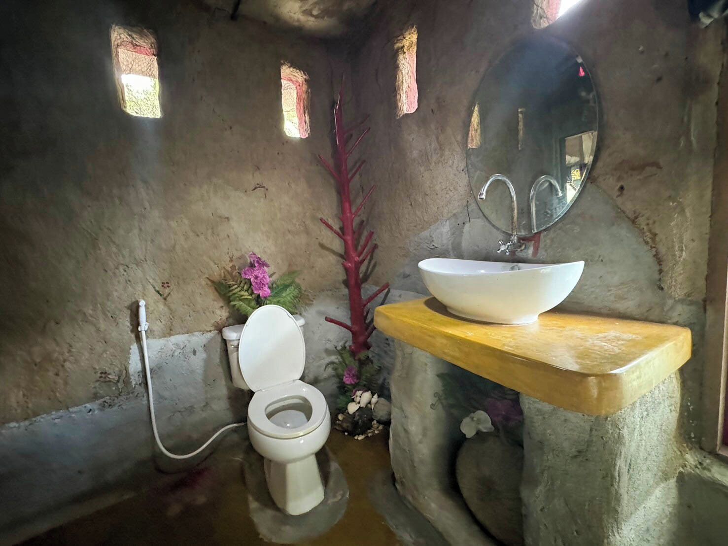 Un baño rústico con un inodoro blanco, un estante de madera que sostiene un lavabo blanco y un espejo sobre el lavamanos.
