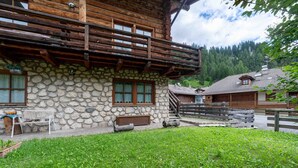 A rustic stone building with a wooden balcony, a bench, and a grassy yard.