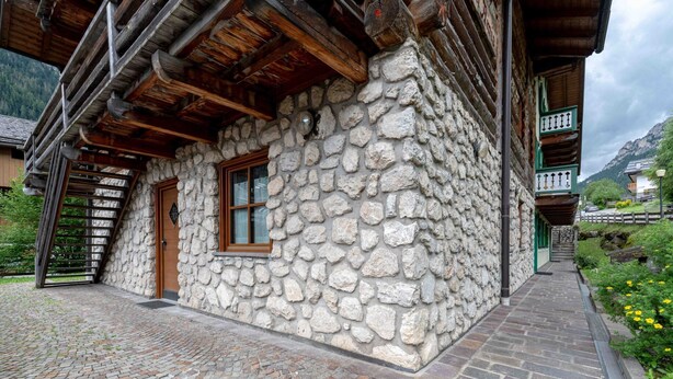 A stone building with a wooden staircase leading to a door, a window, and a stone wall.