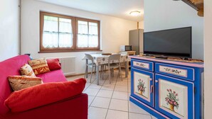 A cozy living room with a red sofa, a dining table, and a TV on a cabinet.