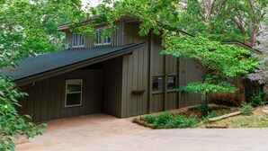 A two-story house with a sloped roof, a covered garage, and a front yard with trees and shrubs.