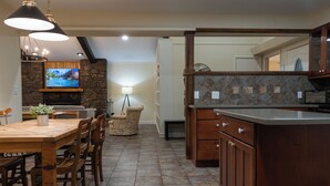 A spacious kitchen with a stone fireplace, wooden dining table, and modern cabinetry.