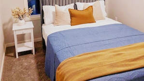 Une chambre bien rangée, avec un lit, une table de chevet et une petite fenêtre.