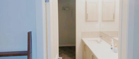 A narrow hallway leading to a bathroom with a sink and mirror.