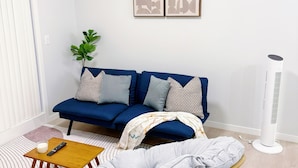 Un salon avec un canapé bleu, un fauteuil en osier, une petite table et un radiateur portatif.