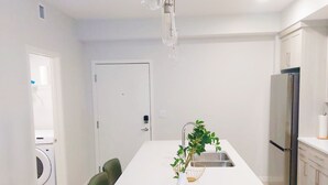 Une cuisine moderne dotée d’un îlot central, d’appareils électroménagers en acier inoxydable et d’un luminaire suspendu.