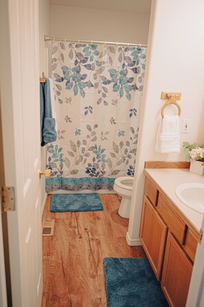 Une salle de bain avec un rideau de douche, des toilettes, un lavabo et des meubles en bois.