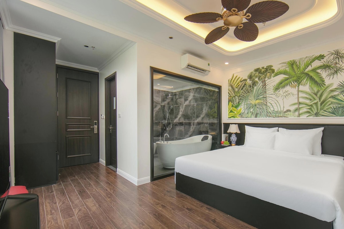 A hotel room with a large bed, a ceiling fan, a bathtub, and a mural of tropical plants.