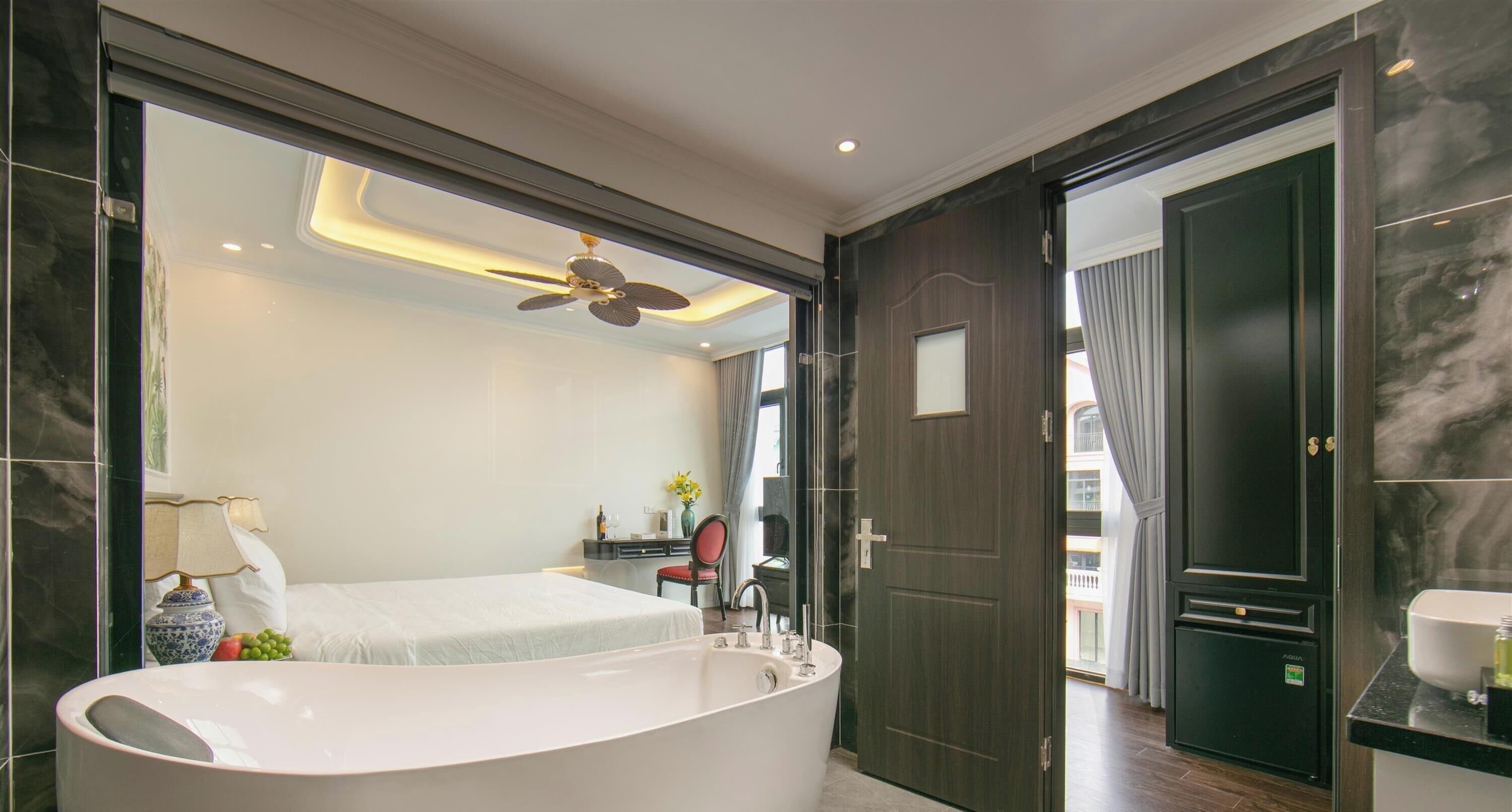 A modern bathroom with a freestanding bathtub, a ceiling fan, and a view into the bedroom.