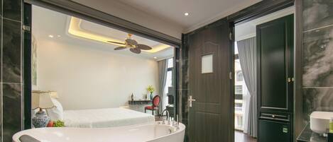 A modern bathroom with a freestanding bathtub, a ceiling fan, and a view into the bedroom.