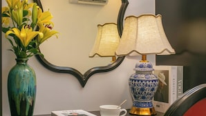 A desk with a vase of yellow flowers, a blue and white lamp, a white cup, and a magazine. - Royal Hotel - Vinhomes Ocean Park 3 (Nghia Tru)