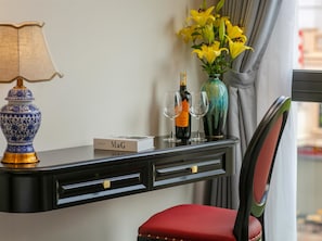 A hotel room with a desk, a red chair, a lamp, a vase with yellow flowers, and a bottle of champagne. - Royal Hotel - Vinhomes Ocean Park 3 (Nghia Tru)