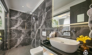 A modern bathroom with a large white sink, a glass shower enclosure, and a marble backsplash. - Royal Hotel - Vinhomes Ocean Park 3 (Nghia Tru)