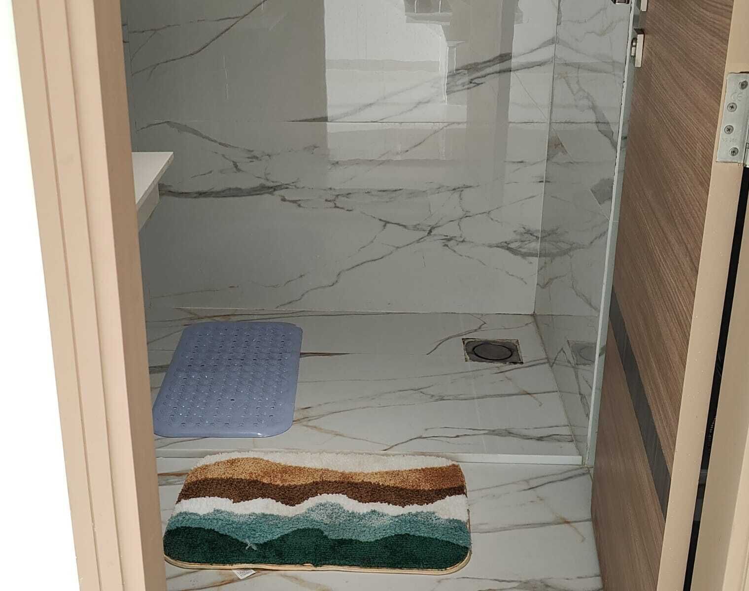 Ein Badezimmer mit Duschbereich, einem blauen Duschhandstück und einer farbenfrohen Badmatte.