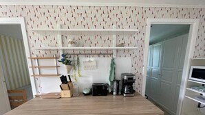 Una cocina con encimera de madera, armarios blancos y una planta colgante. Hay repisas sobre la encimera y un microondas a la derecha.