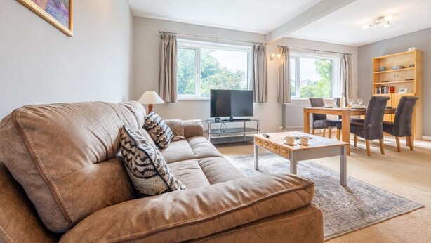 A living room with a brown leather sofa, a TV, a dining table with chairs, and a bookshelf. - Charming 2-Bed Detached Home in Radyr (Cardiff)