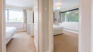 A hotel room with a bed, a small desk, a radiator, and a window with curtains. - Charming 2-Bed Detached Home in Radyr (Cardiff)