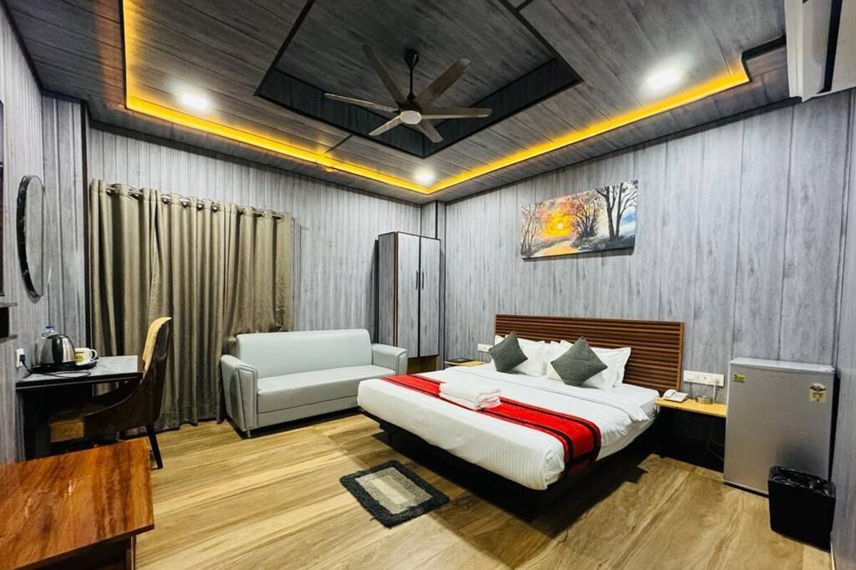 A modern hotel room with a bed, a desk, a chair, a sofa, and a ceiling fan.