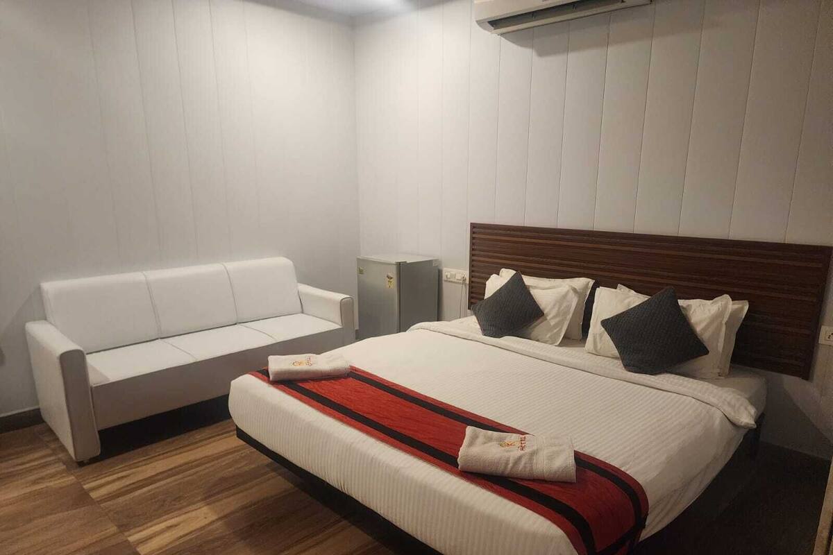A hotel room with a bed, a white sofa, and a wooden floor.