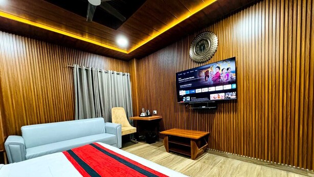 Habitación de hotel con cama, sofá, televisor montado en la pared y paneles de madera decorando las paredes.