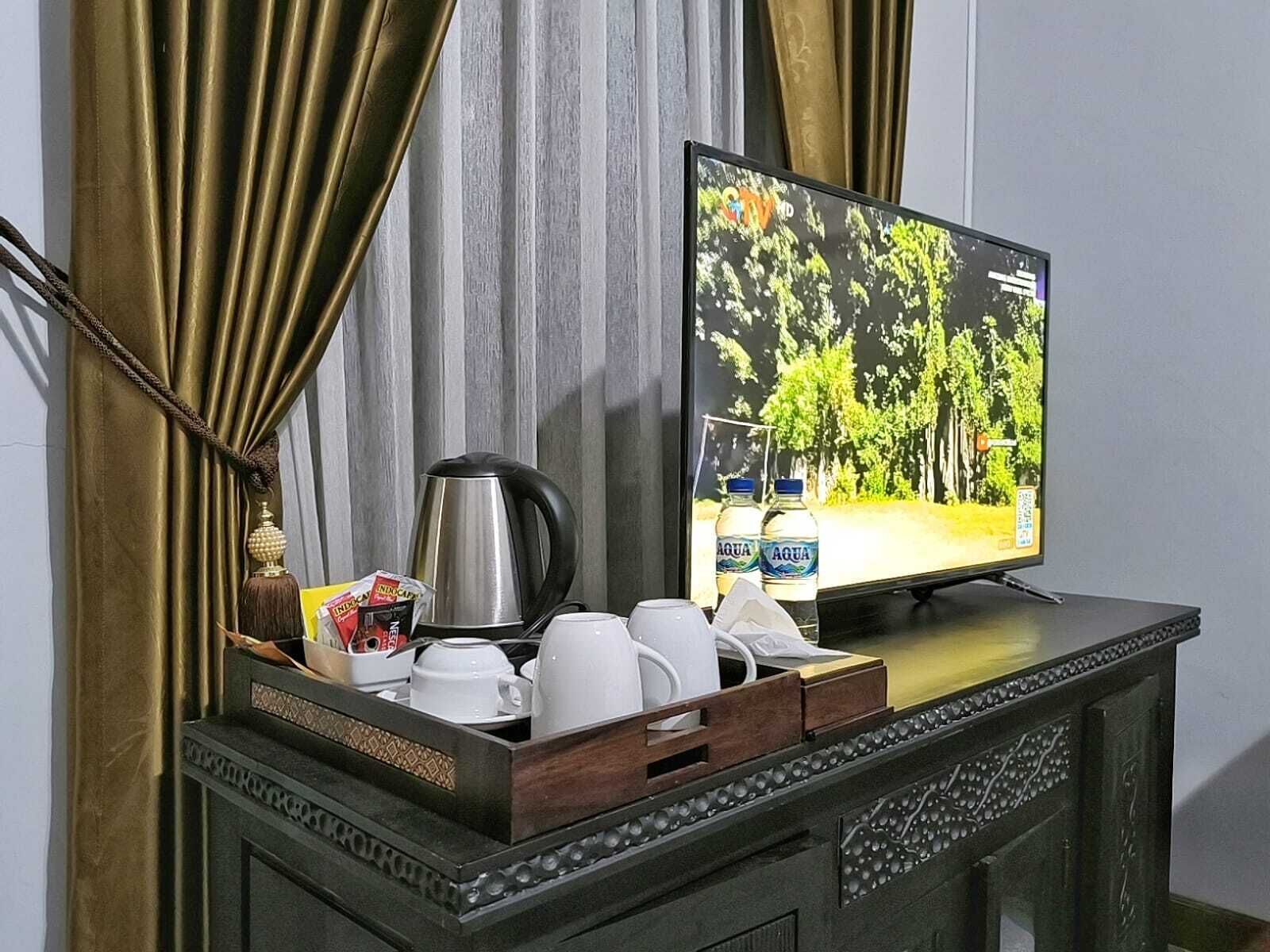Un televisor sobre un mueble de madera con una cafetera, tazas y una botella de agua.
