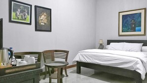 Habitación de hotel con cama, escritorio con hervidor, sillas y cuadros en la pared.