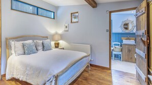 Ein Schlafzimmer mit einem hölzernen Bett, einer Nachttischlampe, einem Heizkörper und Blick in einen weiteren Raum mit Waschbecken und Spiegel.