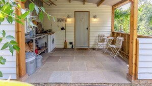 Eine überdachte Veranda mit Waschmaschine, Besen und einem Schild mit der Aufschrift 'GARDEN'.