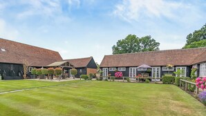 A courtyard with a lawn, two buildings with brick roofs, and a clear sky. - Weston Cottage - UK50016 (Woking, near Guildford)