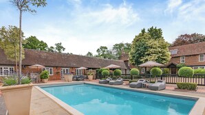 A swimming pool with lounge chairs, a brick building, and a fenced garden area. - Weston Cottage - UK50016 (Woking, near Guildford)