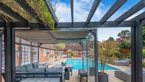 A covered outdoor seating area with a pool, brick walls, and potted plants. - Weston Cottage - UK50016 (Woking, near Guildford)