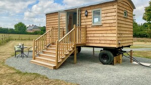 A wooden mobile home with a staircase leading to a door, a small table with a chair, and a window. - 1 bedroom accommodation in Southtown, nr Illminster (Southtown, nr Illminster)