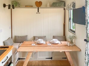 Un coin repas avec une table en bois dressée pour deux personnes, des murs blancs et un téléviseur fixé au mur.