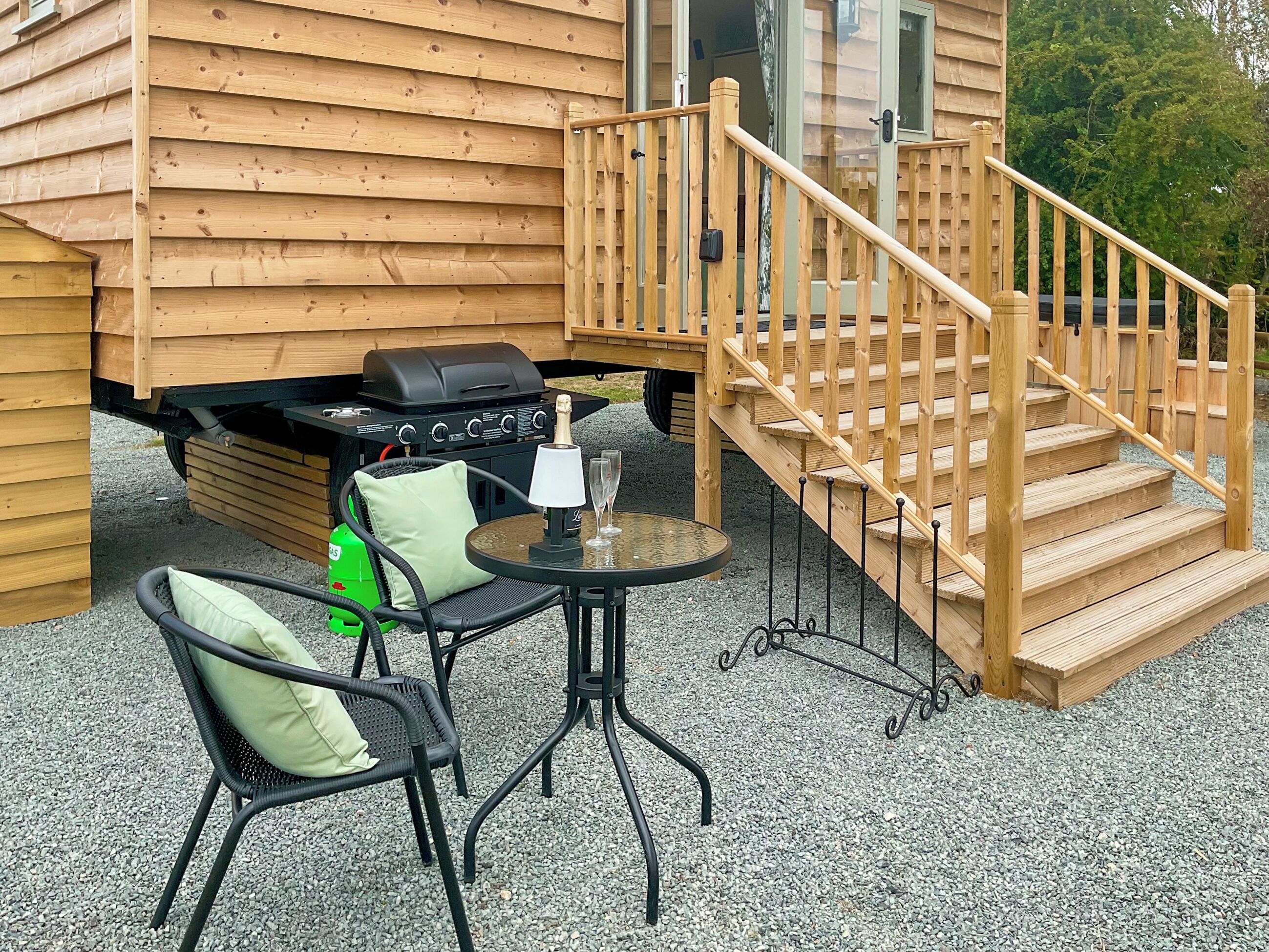 A wooden deck with a grill, a table with chairs, and a staircase leading to a cabin.