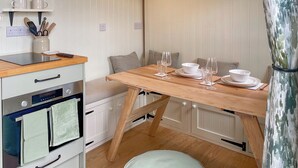 A compact kitchen with a wooden table set for dining, a small round ottoman, and a white cabinet with a built-in oven. - 1 bedroom accommodation in Southtown, nr Illminster (Southtown, nr Illminster)