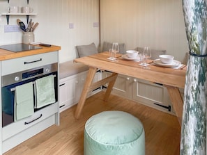 A compact kitchen with a wooden table set for dining, a small round ottoman, and a white cabinet with a built-in oven.