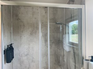 A modern shower enclosure with a glass door, a handheld showerhead, and a wall-mounted control panel.